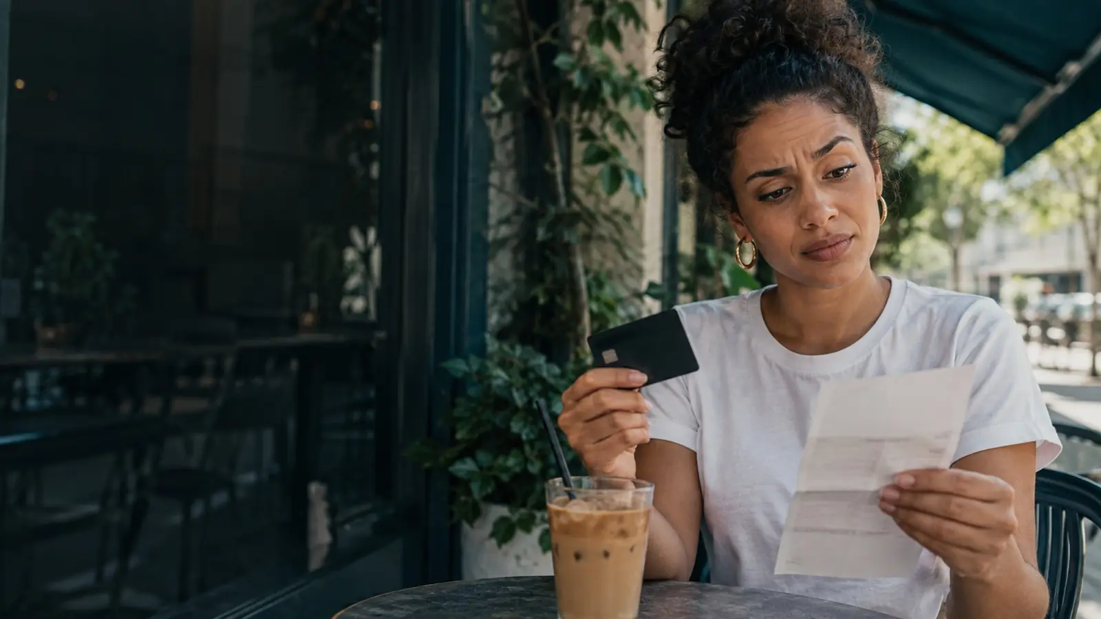 Mulher em um café com o cartão de crédito e a fatura na mão, surpresa com a anuidade